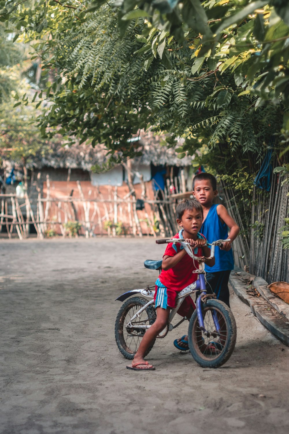 Dos niños de pie junto a la bicicleta cerca de una choza