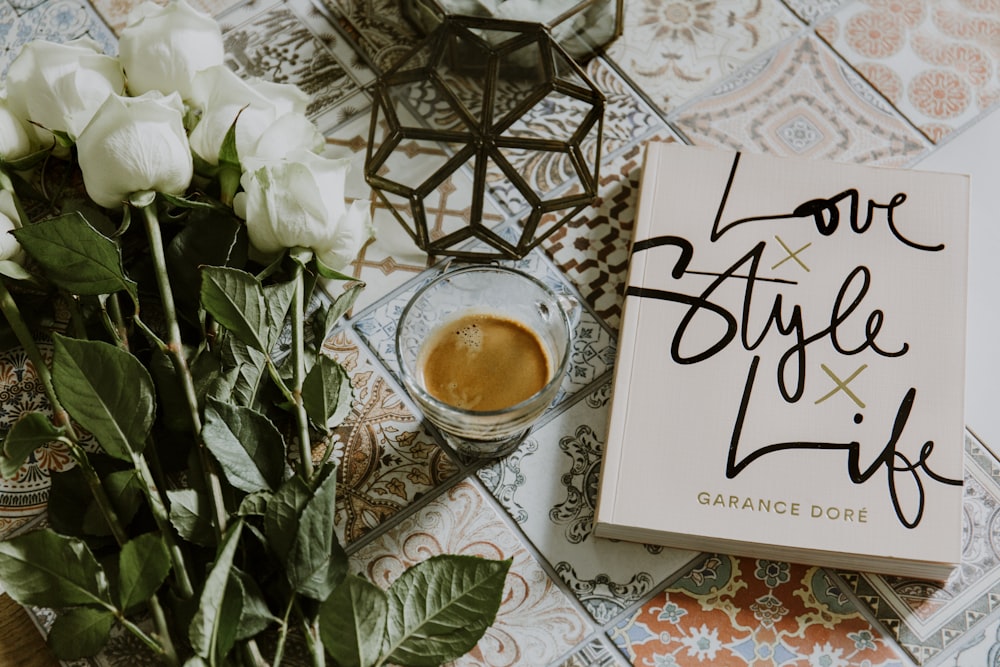 clear glass cup filled with coffee near white roses and book