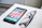 A smartphone with a colorful display of app icons is placed on a white surface next to a pair of black-framed eyeglasses.