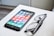 A smartphone with a colorful display of app icons is placed on a white surface next to a pair of black-framed eyeglasses.