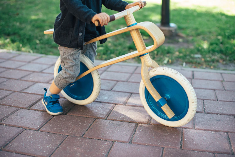 A toddler riding a wooden balance bike on paving stones
