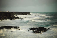 A dynamic video still of waves crashing against rocky cliffs under a cloudy sky.