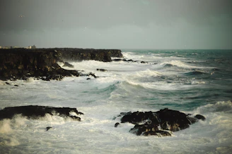 A dynamic video still of waves crashing against rocky cliffs under a cloudy sky.