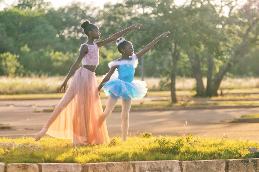 two girls wearing blue and peach dresses dancing on green grass