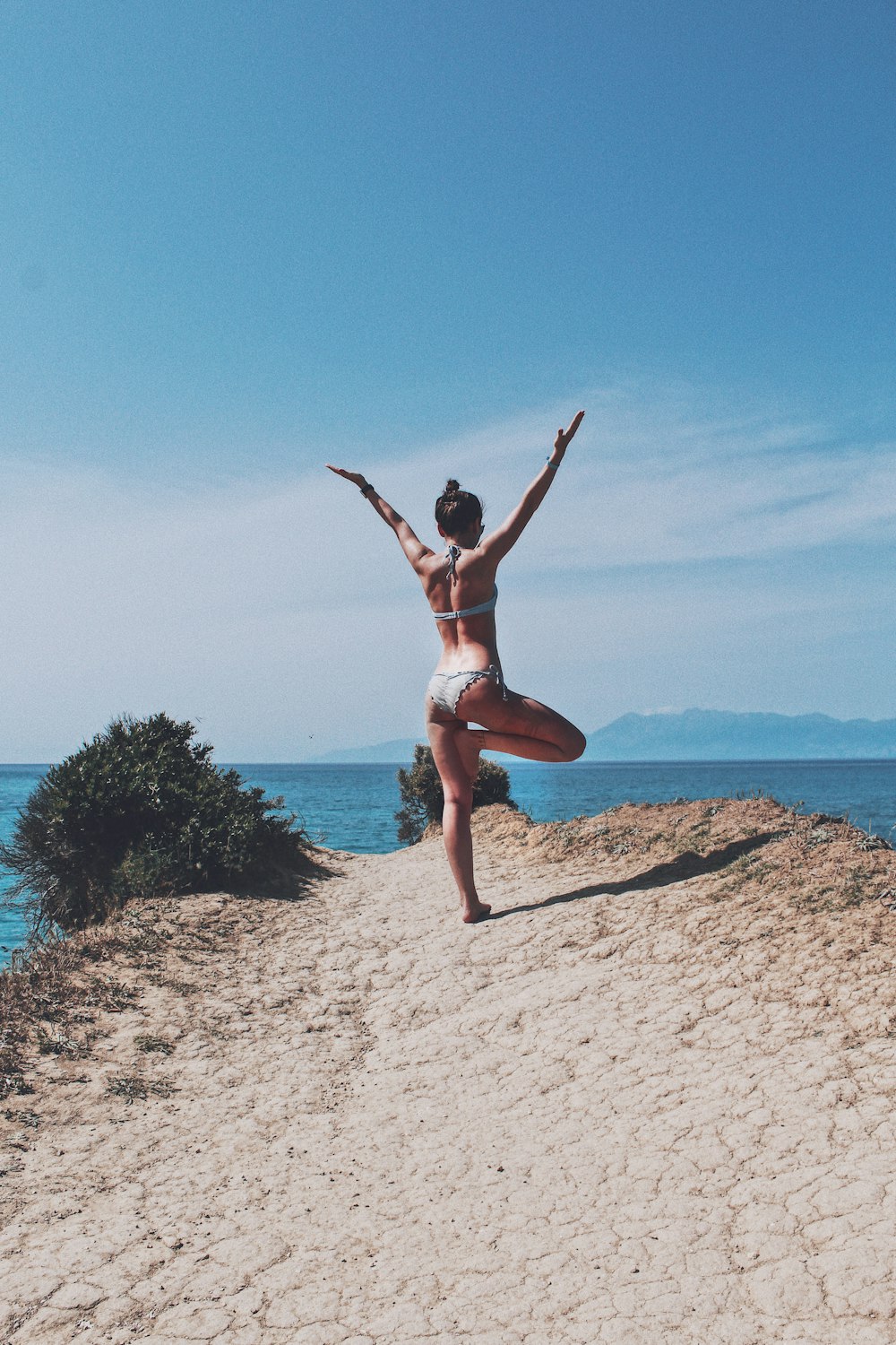 a woman in a bikini doing a yoga pose on a beach