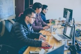 three men facing computer monitors