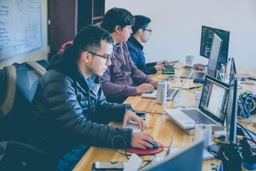three men facing computer monitors