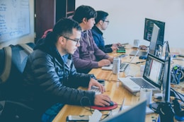 three men facing computer monitors