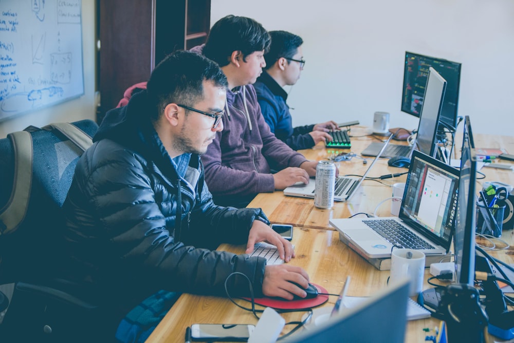 three men facing computer monitors