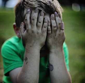 boy sitting while covering his face