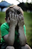 boy sitting while covering his face