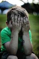 boy sitting while covering his face