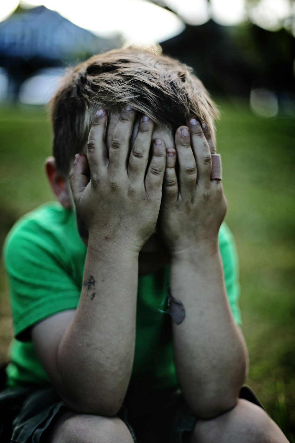 boy sitting while covering his face