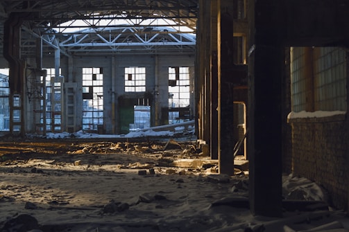 A misty abandoned factory hall with broken windows and scattered debris.