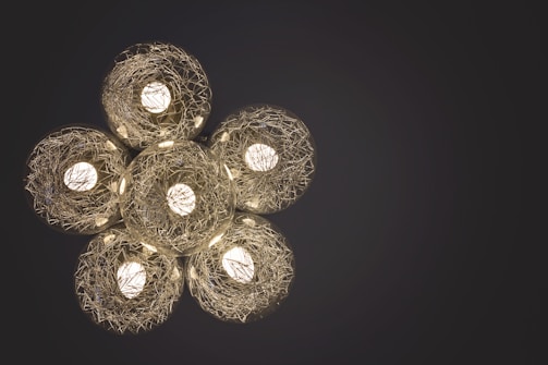 Five spherical light fixtures with intricate wire designs encase glowing bulbs, arranged in a flower-like pattern against a dark background.