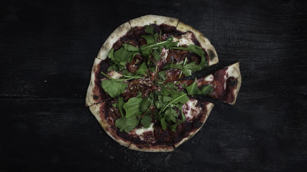 a pizza topped with greens and meat on a wooden table