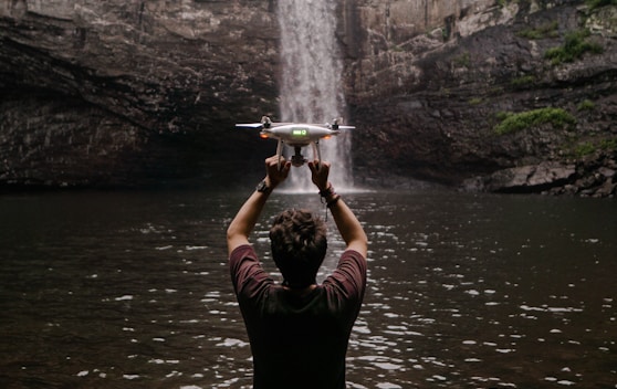 man holding drone facing waterfalls