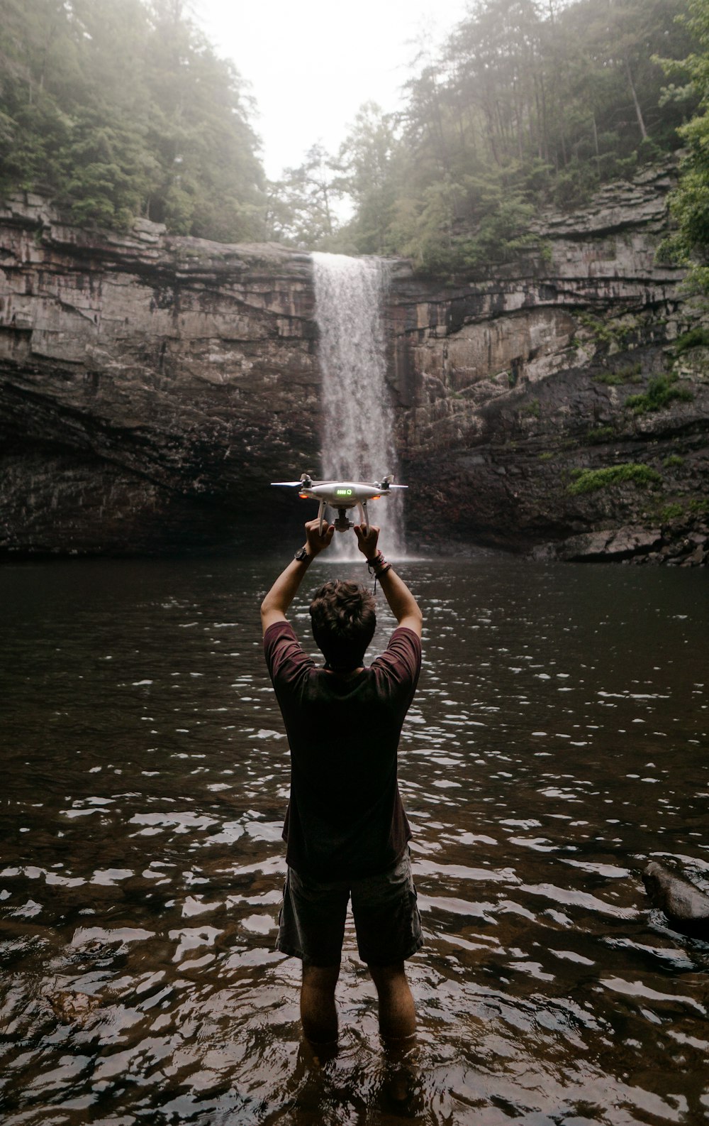 man holding drone facing waterfalls