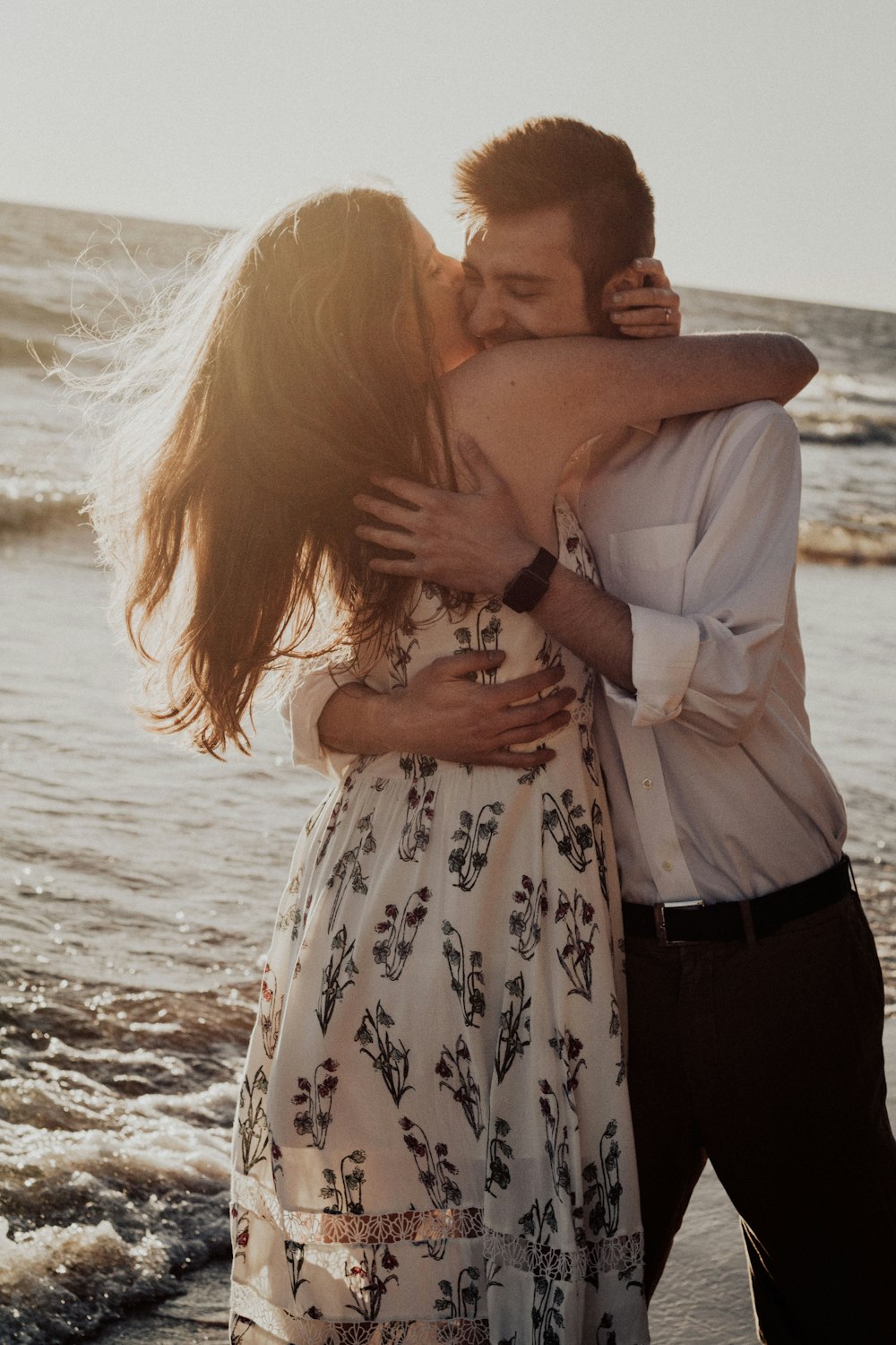woman hugging and kissing man on cheek on seashore during daytime