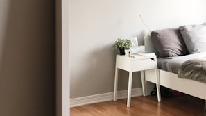 A serene bedroom corner with neutral-toned linens and a small potted plant on the nightstand.