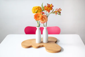 A set of bright, hand-thrown ceramic vases arranged with fresh wildflowers on a rustic wooden bench
