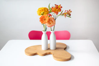A set of bright, hand-thrown ceramic vases arranged with fresh wildflowers on a rustic wooden bench