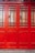 A close-up of a vibrant red wooden door with decorative grid patterns and frosted glass panels. The door features a mix of vertical and horizontal wooden slats, creating a geometric design. The lower section of the door is solid wood, while the upper section is divided by a series of small glass panes.