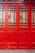 A close-up of a vibrant red wooden door with decorative grid patterns and frosted glass panels. The door features a mix of vertical and horizontal wooden slats, creating a geometric design. The lower section of the door is solid wood, while the upper section is divided by a series of small glass panes.
