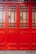 A close-up of a vibrant red wooden door with decorative grid patterns and frosted glass panels. The door features a mix of vertical and horizontal wooden slats, creating a geometric design. The lower section of the door is solid wood, while the upper section is divided by a series of small glass panes.