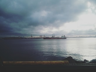 A cargo ship navigating calm ocean waters near a busy port.