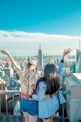 two women hands on their back while raising their hands facing Empire State building