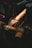A person wearing gloves is sharpening an axe blade on a grinding wheel, with bright sparks flying off as the metal is honed.