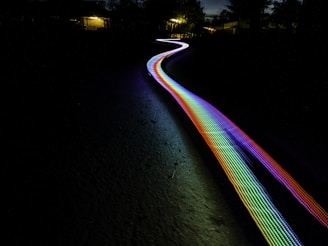 photo: multicolored light path through terrain, with blurry residences in distance