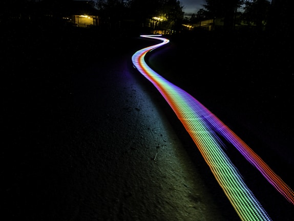 photo: multicolored light path through terrain, with blurry residences in distance