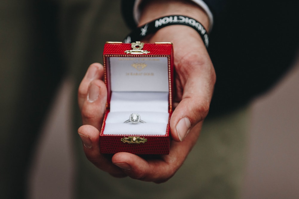 person holding box of silver-colored ring with clear gemstone