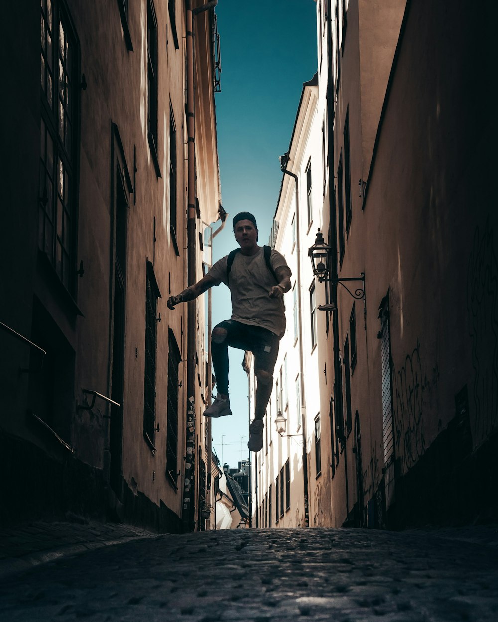 man jumping in middle of brown buildings