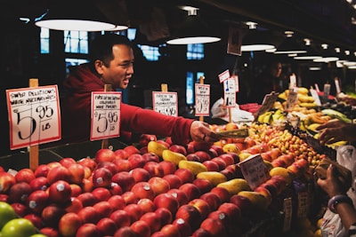 Friendly shopkeeper helping a customer pick fresh fruits at the store counter.