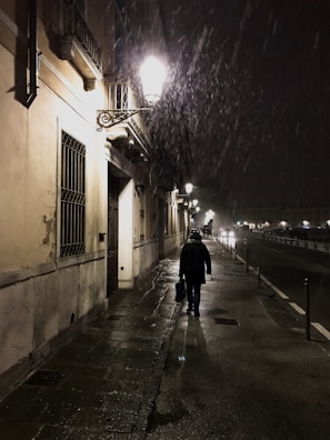 A solitary figure walking through a rain-soaked street.