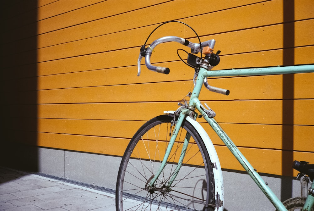 teal road bike parked beside brown wall