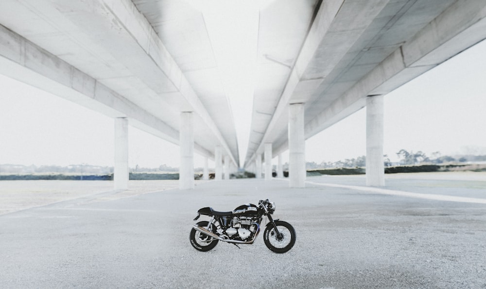 motocicletta nuda nera sotto il ponte bianco durante il giorno