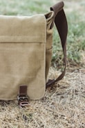 A rugged leather messenger bag resting on a wooden bench outdoors.