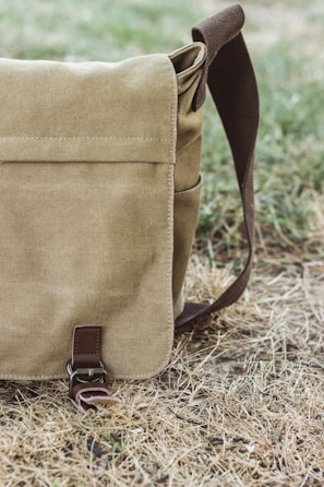 A casual hemp messenger bag resting against a brick wall outdoors.