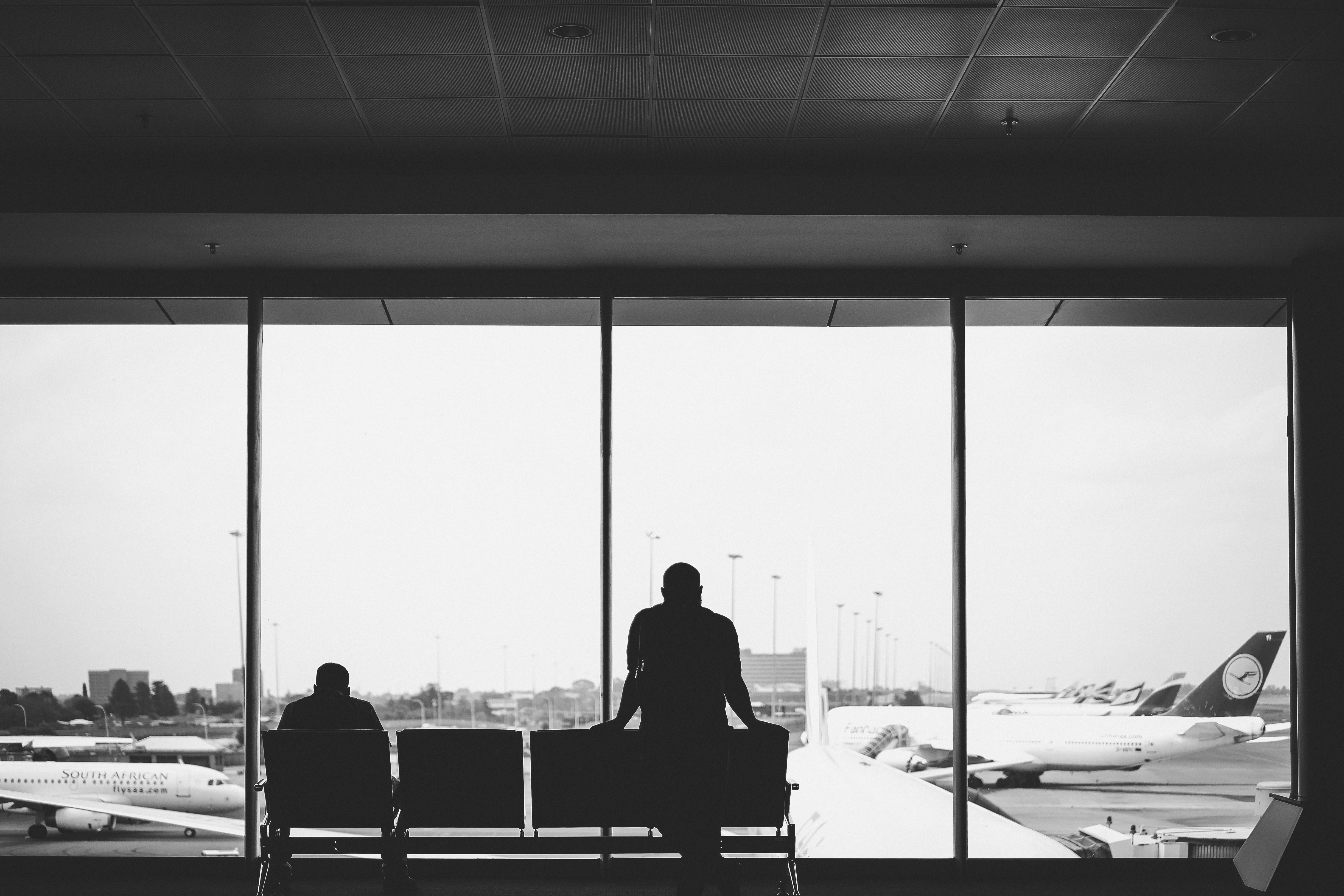 grayscale photography of standing person near sitting person, Captured as I was waiting to board a flight in 2017