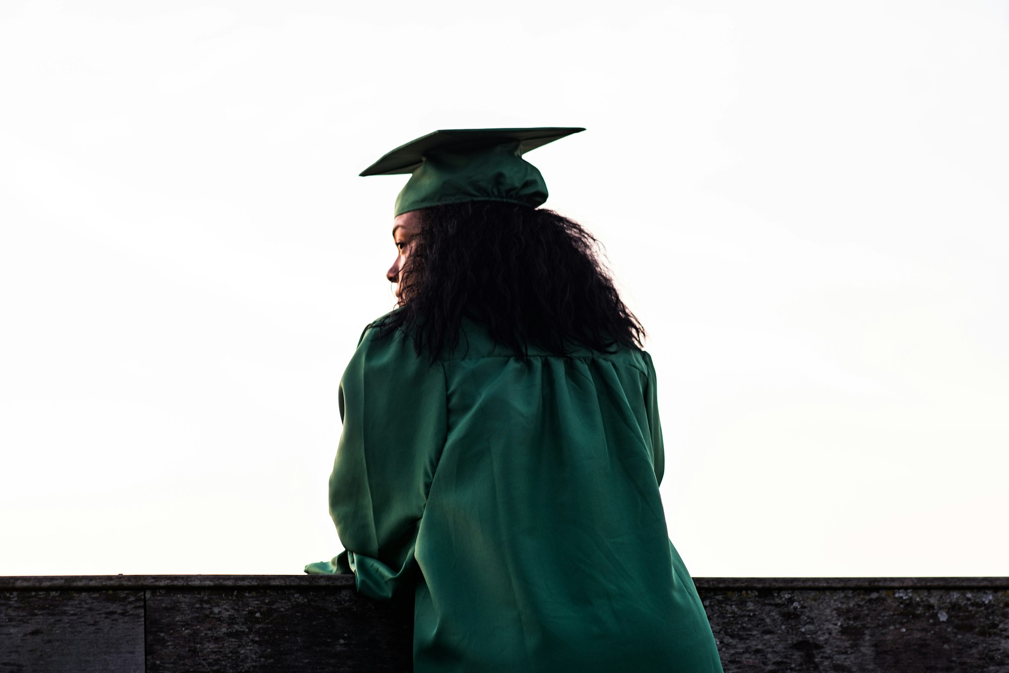 A student in her graduation gown looks out over a wall.