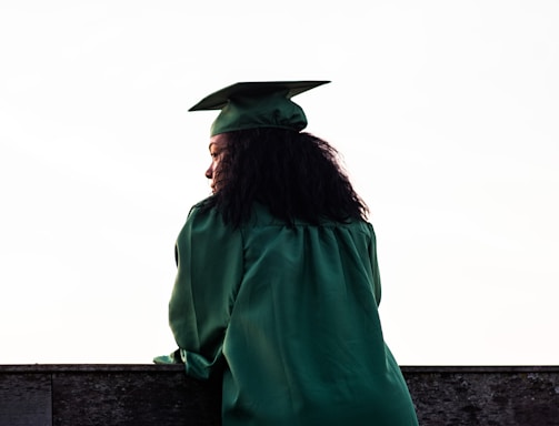 woman standing at front of concrete fence wearing academic uniform