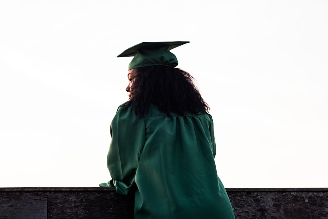 woman standing at front of concrete fence wearing academic uniform, The Graduation