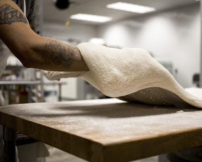 A smiling baker stretching dough by hand before placing it into the oven.