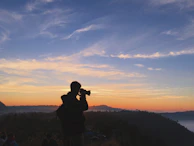 A traveler with camera gear, silhouetted against a golden sunrise over the Tadoba forest.