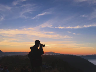 A traveler with camera gear, silhouetted against a golden sunrise over the Tadoba forest.