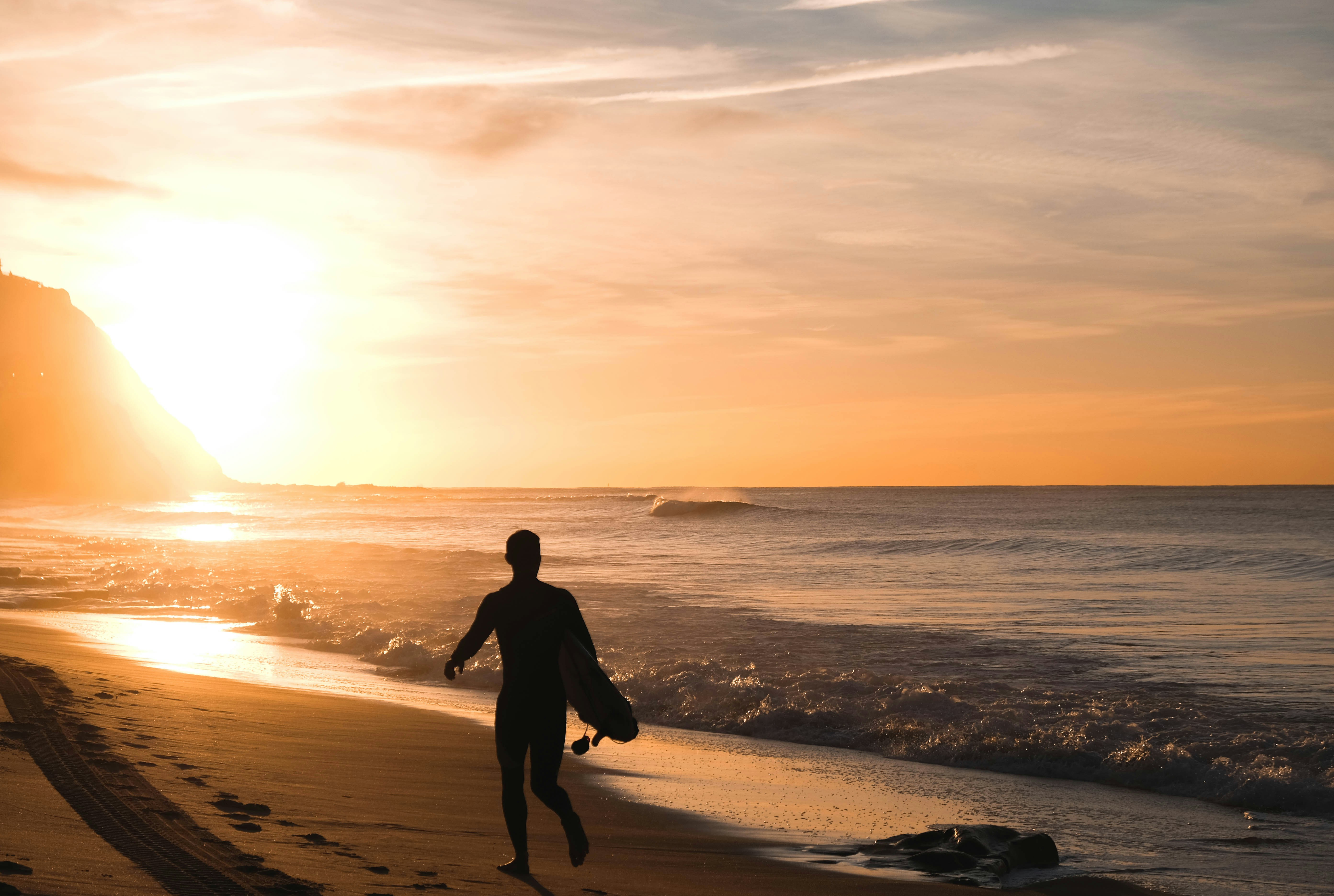 silhouette of man carrying surfboard running on shore, 
